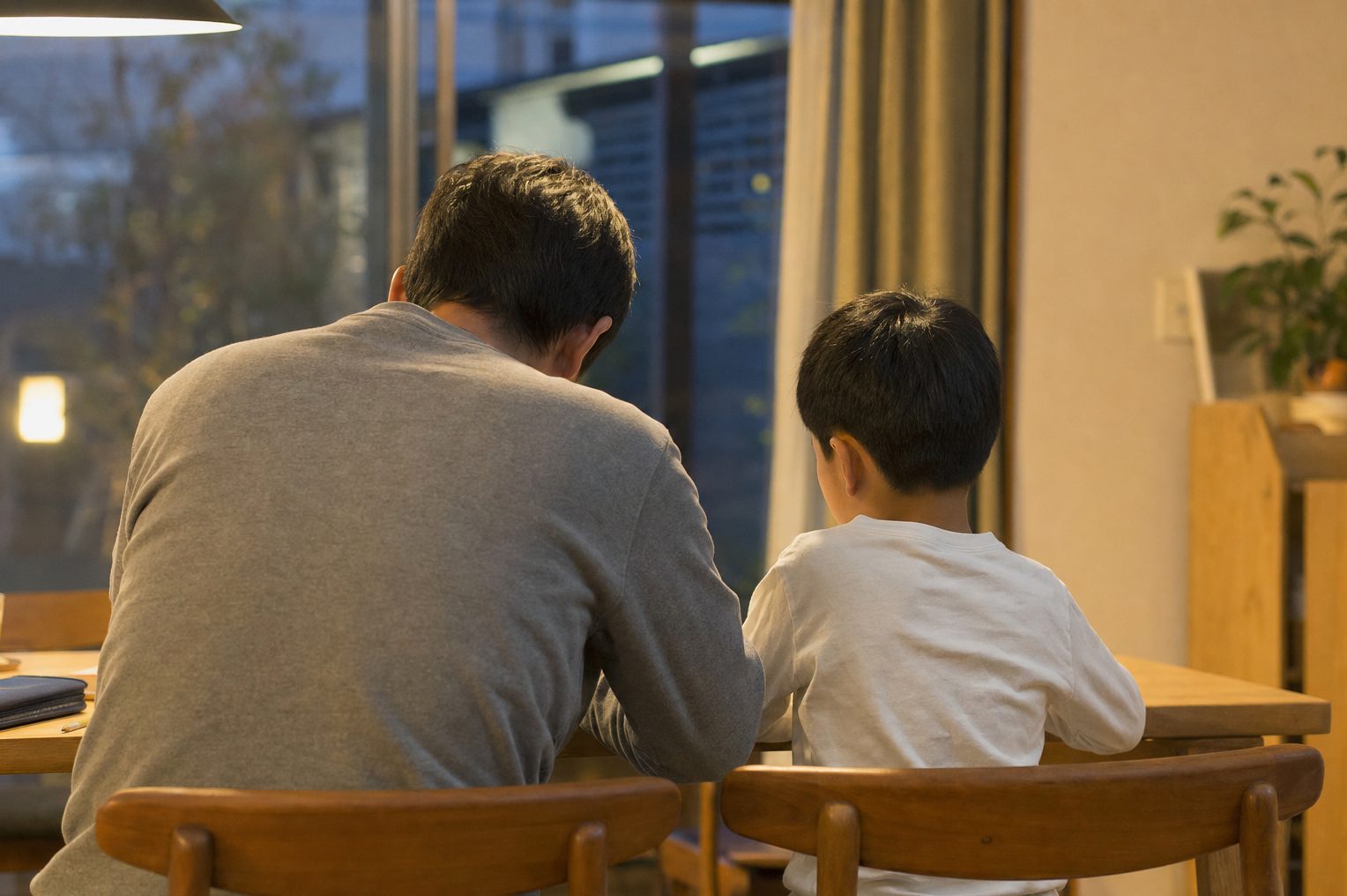 夜のダイニングで穏やかに向き合って話す親子の後ろ姿