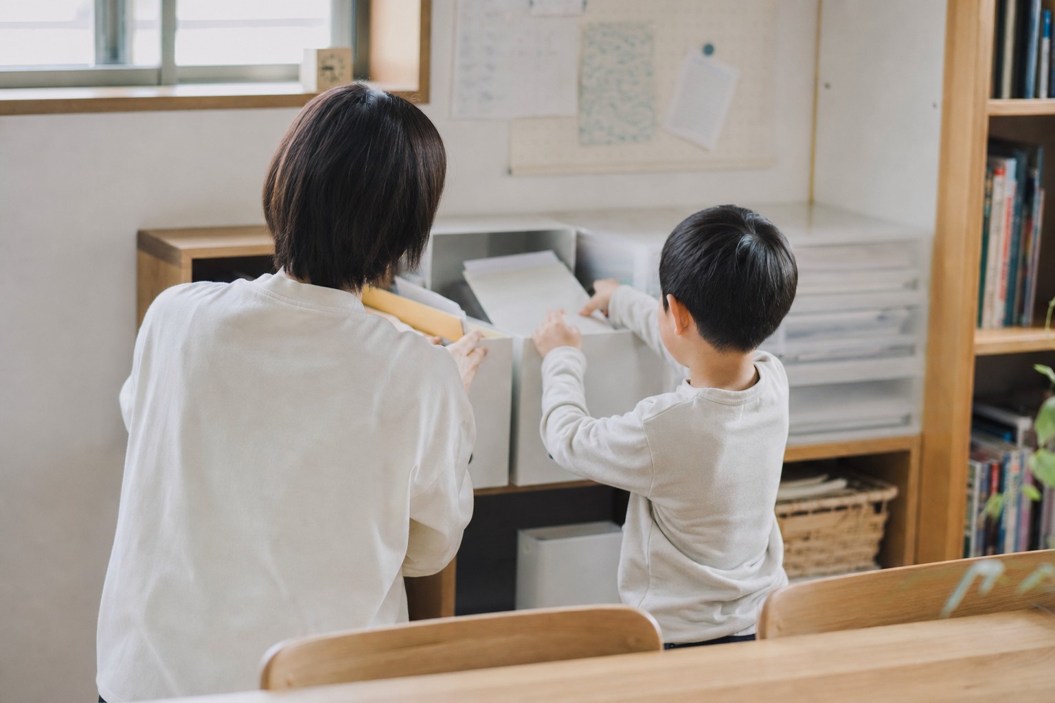 親子で棚のプリントを整理する後ろ姿